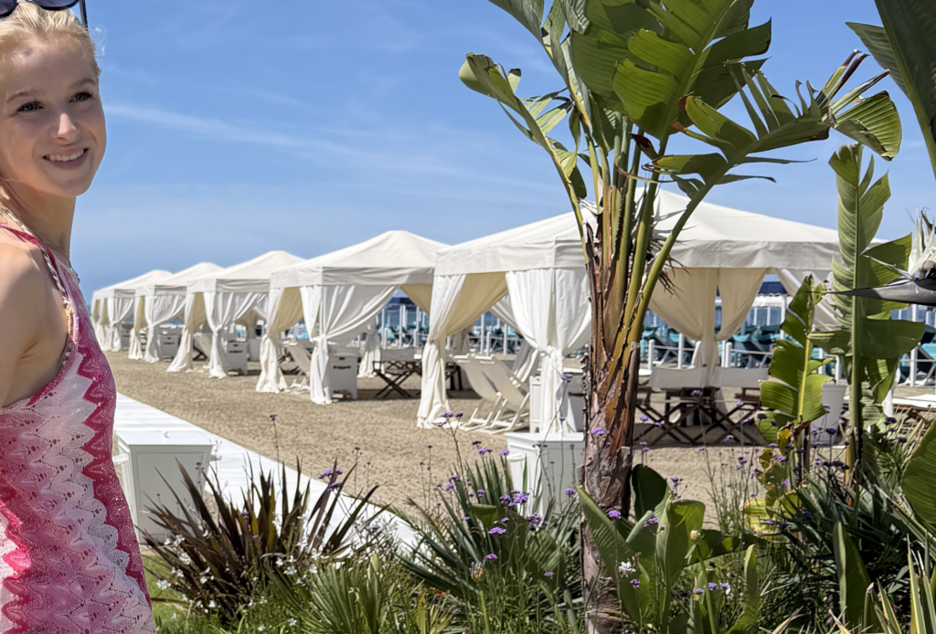 Sonnenschutz nach Botox, nach Filler Sonne, nach Peeling Sonne, Sonnenschutz ästhetische Behandlung, UV-Schutz nach Microneedling. Bild von einer jungen Frau in pinkem Kleid am Strand mit Palmen und Strandzelten