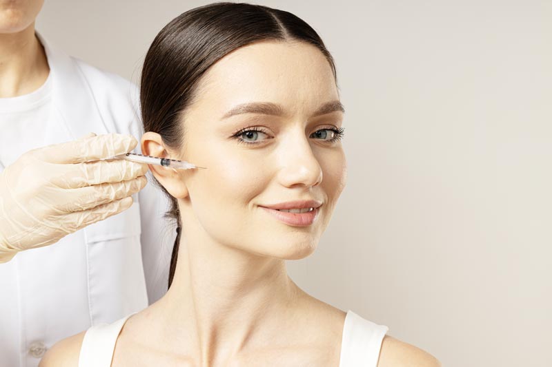 concept-beauty-botox-with-young-woman-2mod Dr. Sarah Ophoff bei der ästhetischen Gesichtsbehandlung in ihrer Praxis am Tegernsee – professionell, einfühlsam und präzise. Sie trägt einen weißen Kittel mit Namensschild. Ihre Haare sind in einem Pferdeschwanze gebunden. Hyaluronsäure Filler Faltenbehandlung