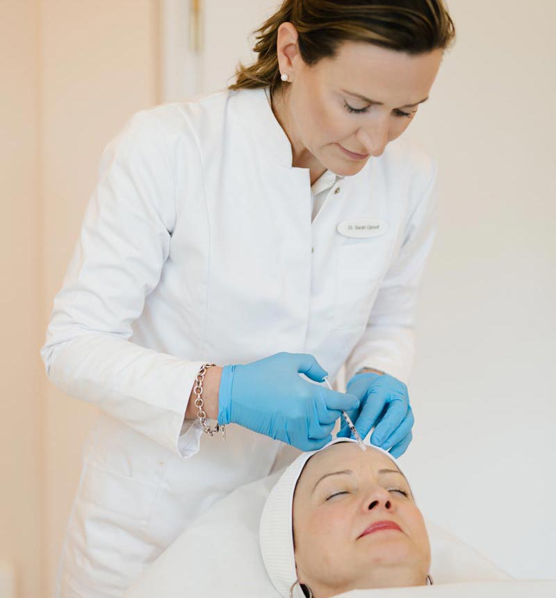 Botox® gegen Zornesfalten: Wie die Behandlung wirkt – und für wen sie geeignet ist. Sarah Ophoff spritzt Botulinumtoxin in die Zornfalte ihrer Patientin - sie hat blaue handschuhe an und einen weißen kittel
